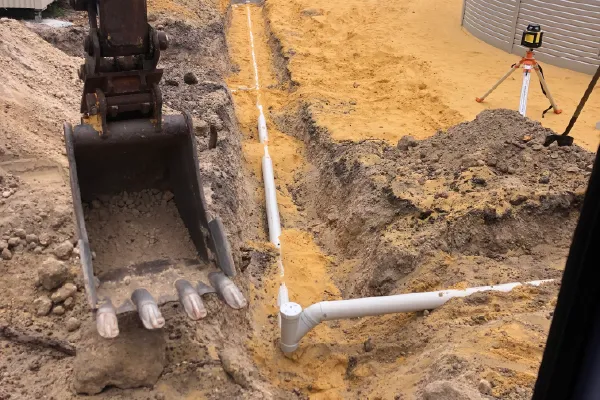 Excavator exposing septic pipework and leach drain during installation works